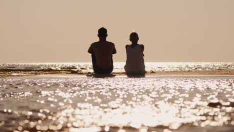 a young couple sits on a sandy island and looks forward to the horizon