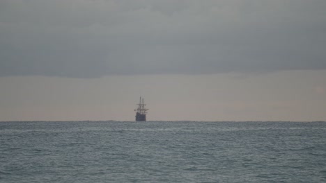 réplica de galeón andaluza del siglo xvi navegando a lo lejos en el mar mediterráneo en un oscuro día nublado al amanecer