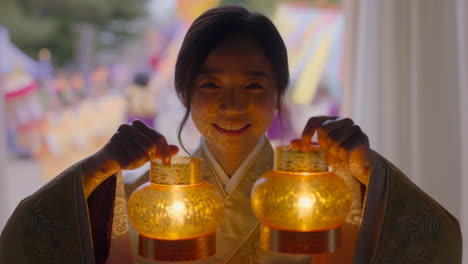 woman smiling and holding two glowing lanterns at a cultural event