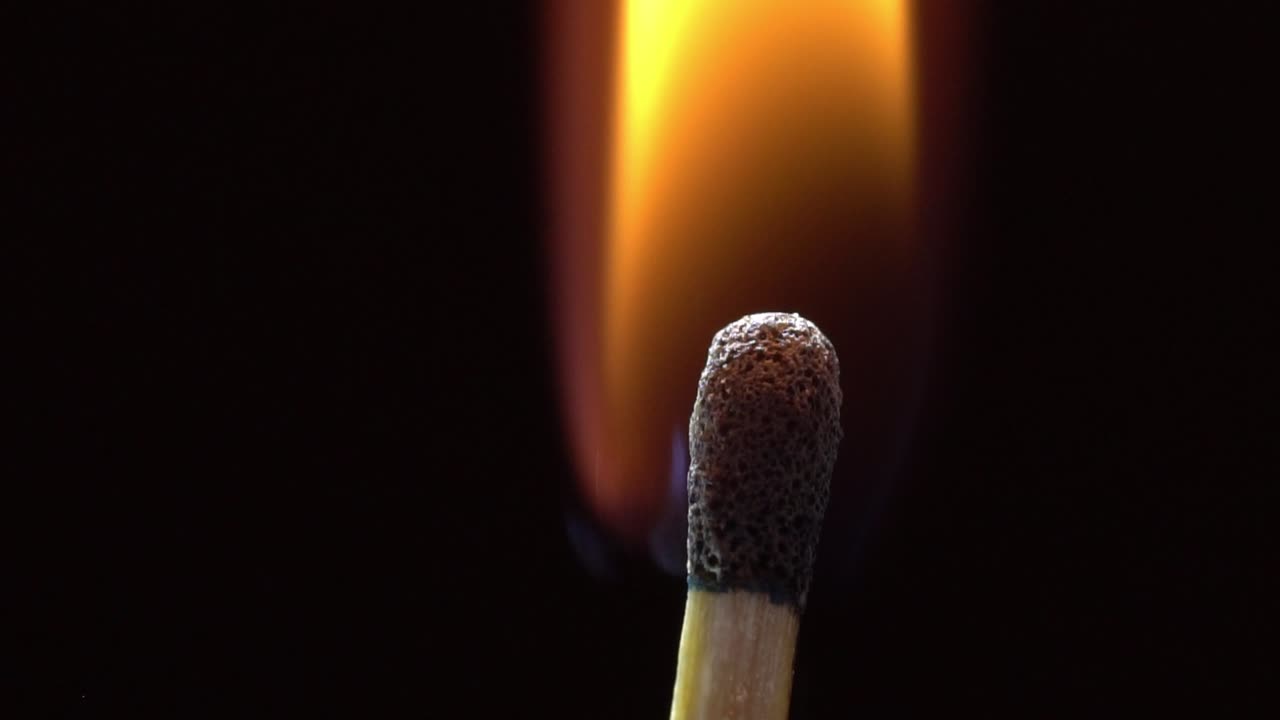 Close-up macro shot of a single matchstick igniting and burning against a dark background