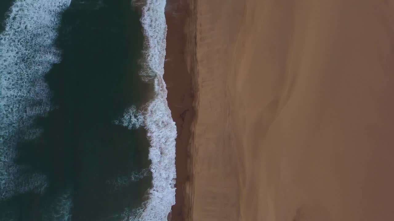 Ripresa aerea con drone a volo d'uccello di Sandwich Harbour in Namibia - il drone sta seguendo la costa dove il deserto incontra l'oceano