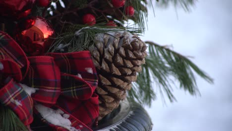 Ornamental-winter-pine-cone-decoration-covered-in-snow-with-pine-needles-in-background-and-white-covered-snow-ground-during-the-decorative-winter-season