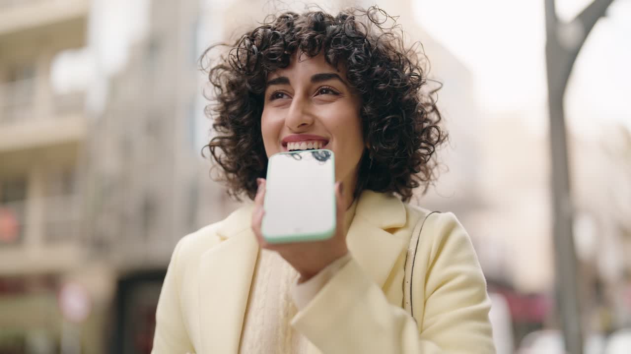 mujer joven sonriendo confiada hablando en el teléfono inteligente en la calle