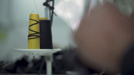 closeup of a tailor manufacturing clothing, spools of cotton in sweatshop factory