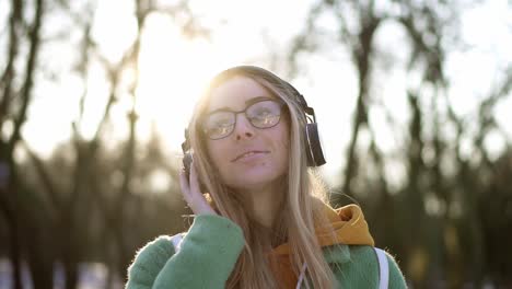 retrato de una mujer en winter park, escuchando música en el teléfono usando auriculares, sonriendo