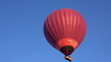 Ein-Roter-Heißluftballon-Steigt-In-Den-Blauen-Himmel,-Während-Der-Pilot-Das-Blasventil-Betätigt