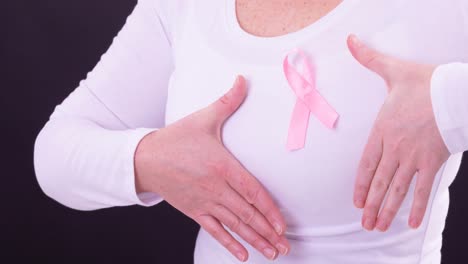 Video-of-midsection-of-caucasian-woman-wearing-pink-cancer-awareness-ribbon,-with-black-background