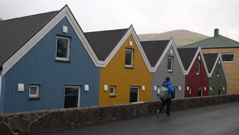 man walking along the colorful wooden cottages in sorvagur, vagar, faroe islands