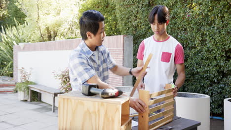 asian father and teenage son working on wooden project together outdoors