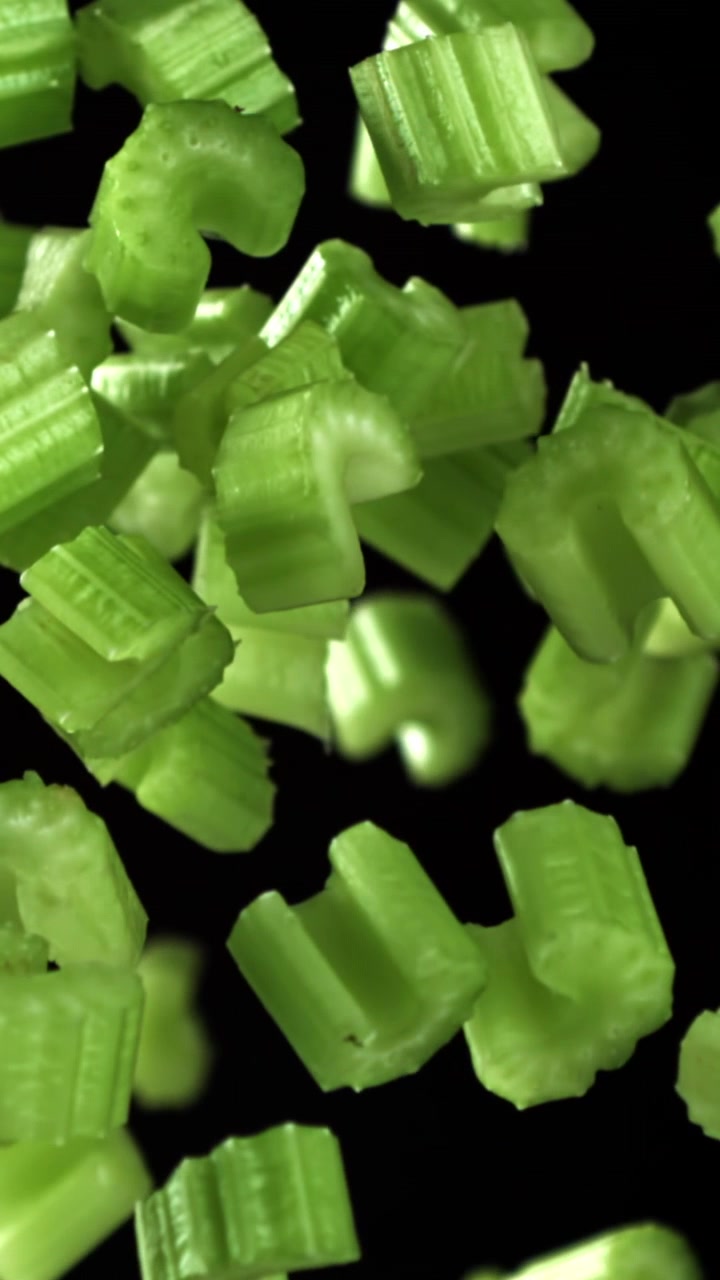 Chopped Green Celery Pieces Falling in Slow Motion on Black Background
