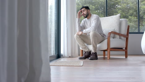 Thoughtful-biracial-man-looking-through-window-at-home,-slow-motion,-copy-space