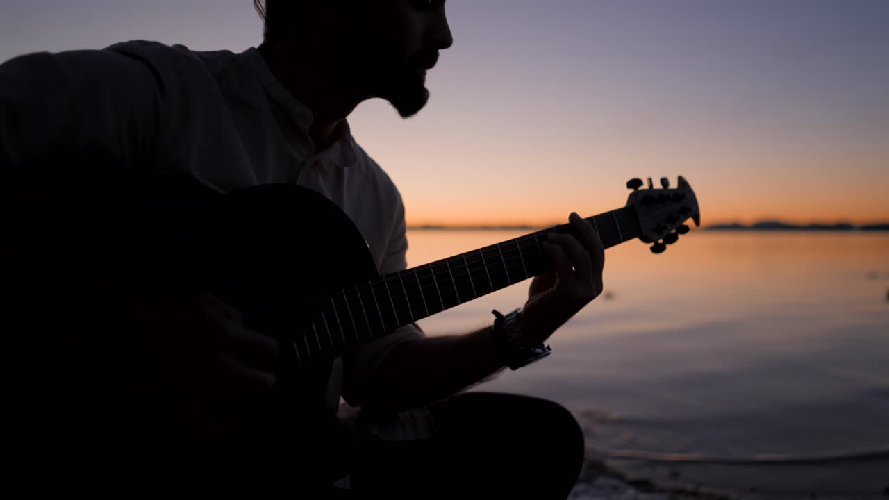 Mann spielt Gitarre bei Sonnenuntergang am See