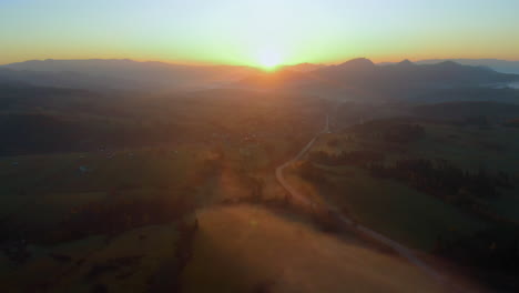 Toma-Aérea-Del-Campo-Polaco-Con-Colinas-Y-Campos-Cubiertos-De-Niebla-Matutina-Con-Amanecer-Amarillo-Y-Cielo-Naranja