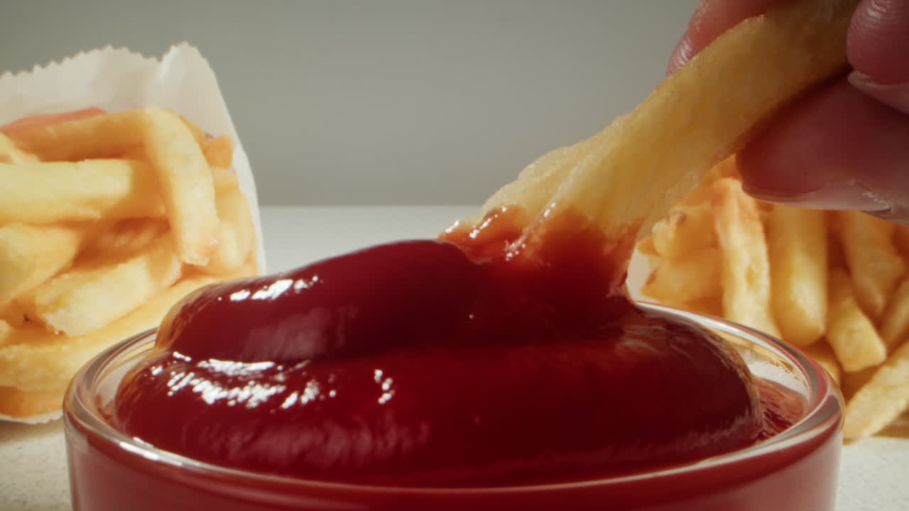 Hand dipping french fries in ketchup