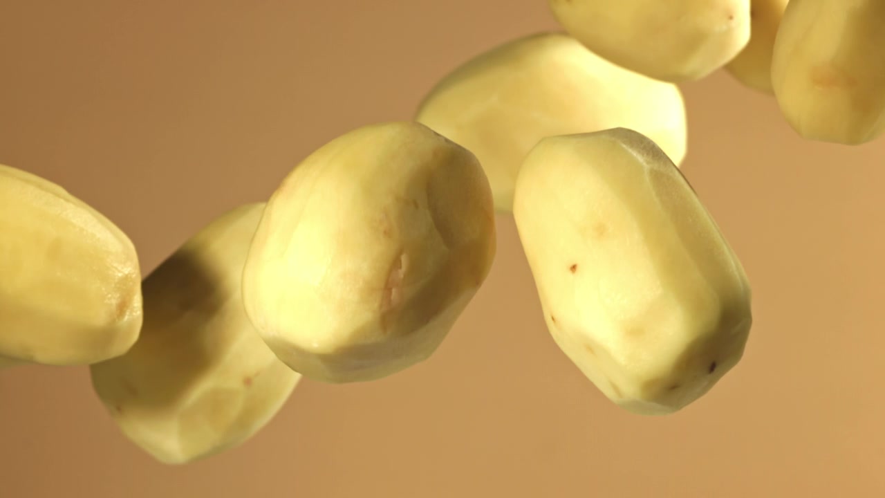 Patate pelate che galleggiano al rallentatore su uno sfondo chiaro