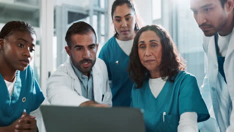 a group of doctors and nurses huddle around a laptop screen, reviewing a patient's case.