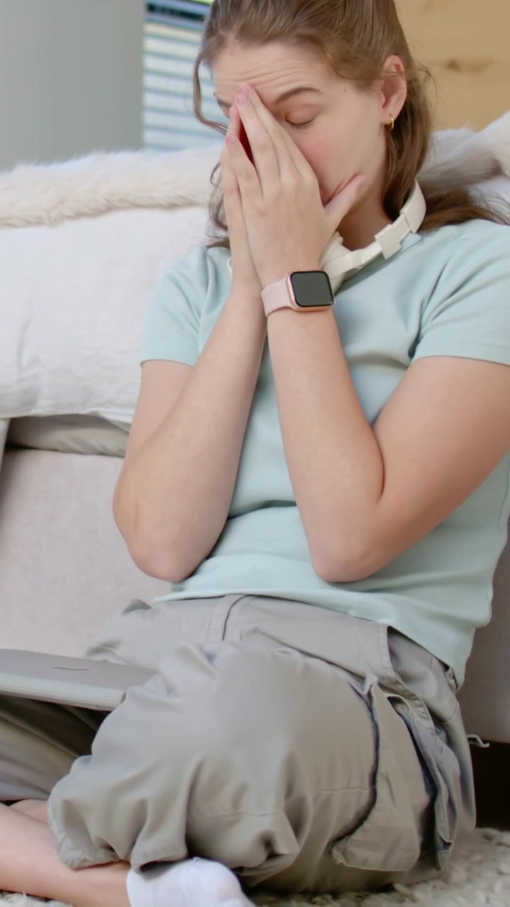 Video verticale: Donna in camicia blu che fa una pausa dal laptop, si strofina gli occhi sul tappeto, smartwatch visibile