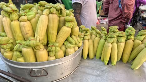 a vendor arranges corn on a cart in a market.