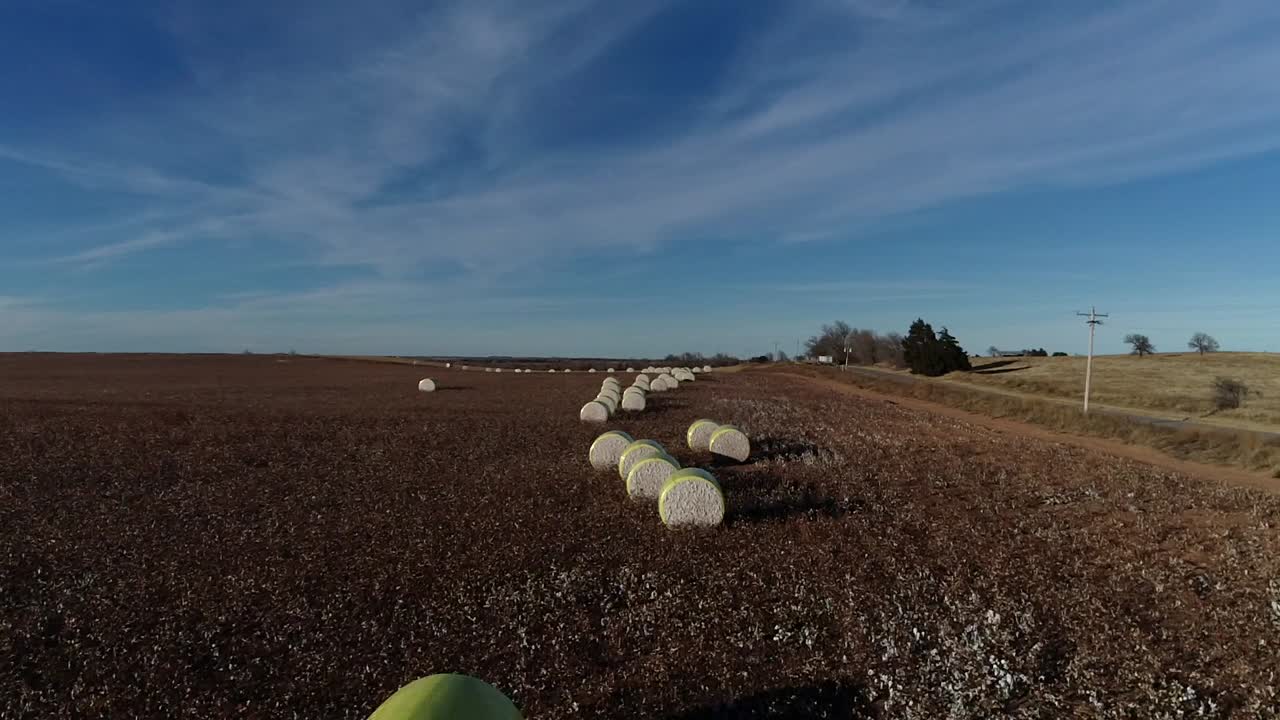 toma aérea de un dron de barrido lento de una granja de algodón del medio oeste con pacas frescas de algodón cosechado envuelto en material amarillo brillante contra un cielo azul abierto