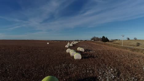 Toma-Aérea-De-Un-Dron-De-Barrido-Lento-De-Una-Granja-De-Algodón-Del-Medio-Oeste-Con-Pacas-Frescas-De-Algodón-Cosechado-Envuelto-En-Material-Amarillo-Brillante-Contra-Un-Cielo-Azul-Abierto