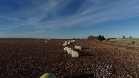 toma aérea de un dron de barrido lento de una granja de algodón del medio oeste con pacas frescas de algodón cosechado envuelto en material amarillo brillante contra un cielo azul abierto