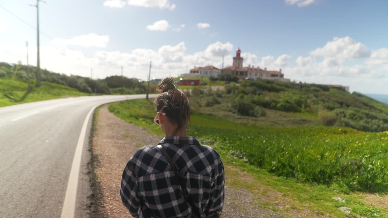 Woman walking along coastal road with lighthouse in the background