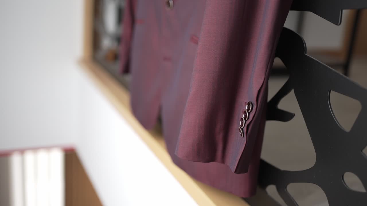 Close up of a burgundy groom’s suit hanging on a modern decorative stand indoors