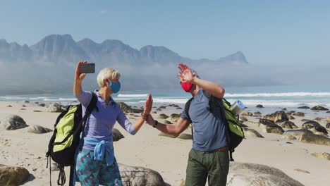 senior hiker couple wearing face masks with backpacks waving while having a videocall on smartphone