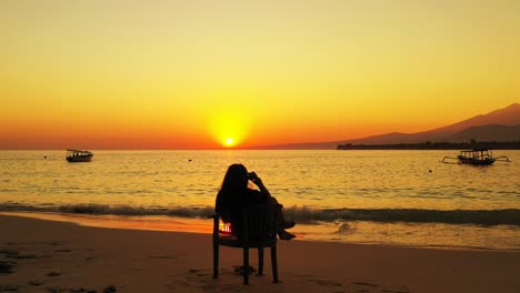 silueta de una chica sentada en la playa al atardecer y usa un smartphone