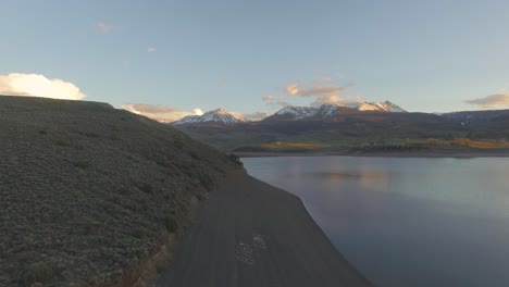 Wunderschöner-Seitlicher-Bildlauf-Bei-Sonnenuntergang-über-Einem-Berghang-In-Schneebedeckten-Felsigen-Bergen-Und-Einem-See