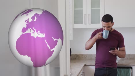 animation of globe spinning and biracial man using smartphone in kitchen