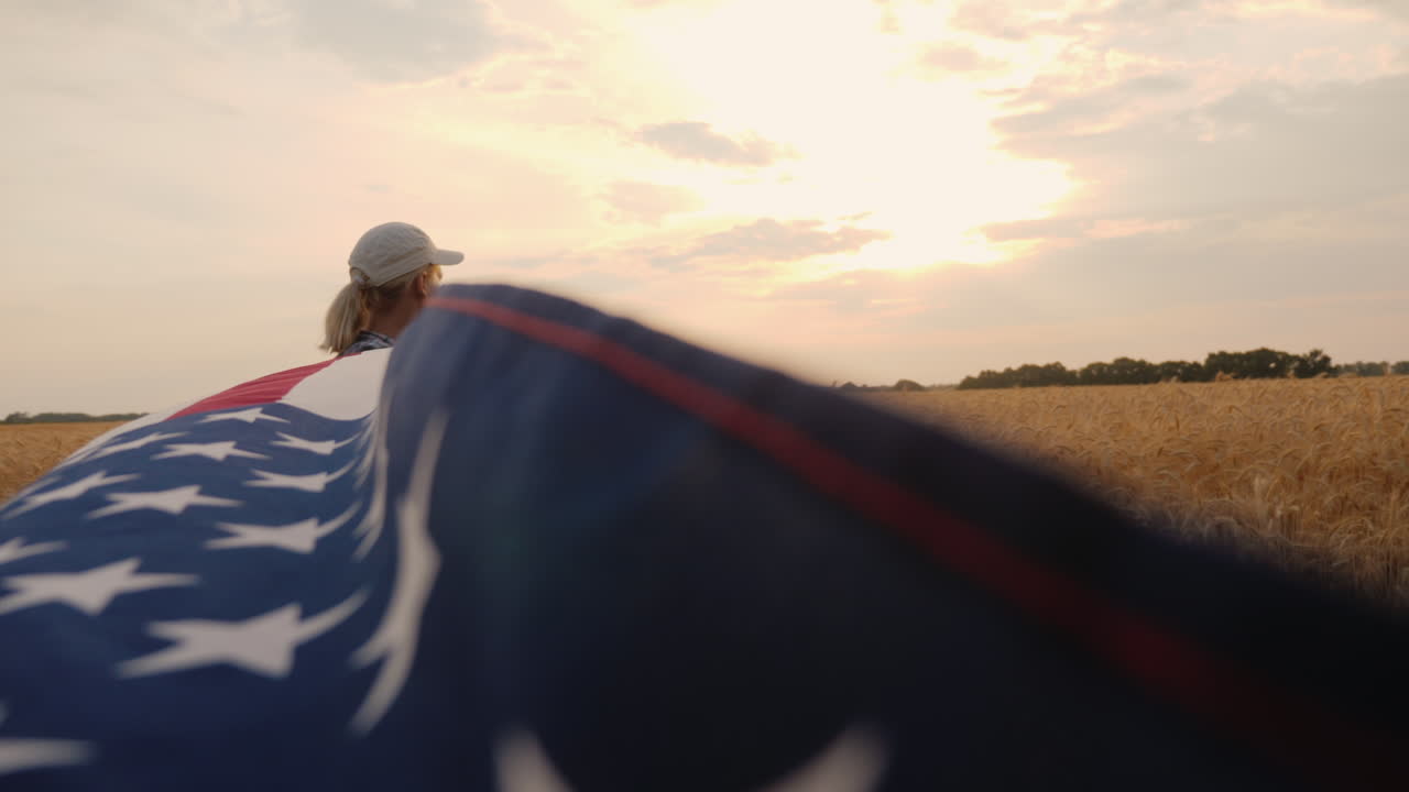 un agricultor patriótico con una bandera estadounidense se encuentra cerca de un campo de trigo maduro sostiene una bandera para uno de los bordes