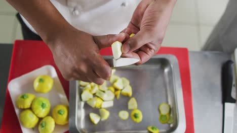 sección media de un cocinero de raza mixta cortando verduras en la cocina de un restaurante