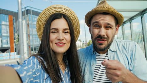 close-up view of caucasian young happy couple of tourists in hats talking, waving hands and smiling at the camera outdoors in summer