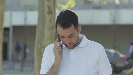 weary young bearded man talking through smartphone.