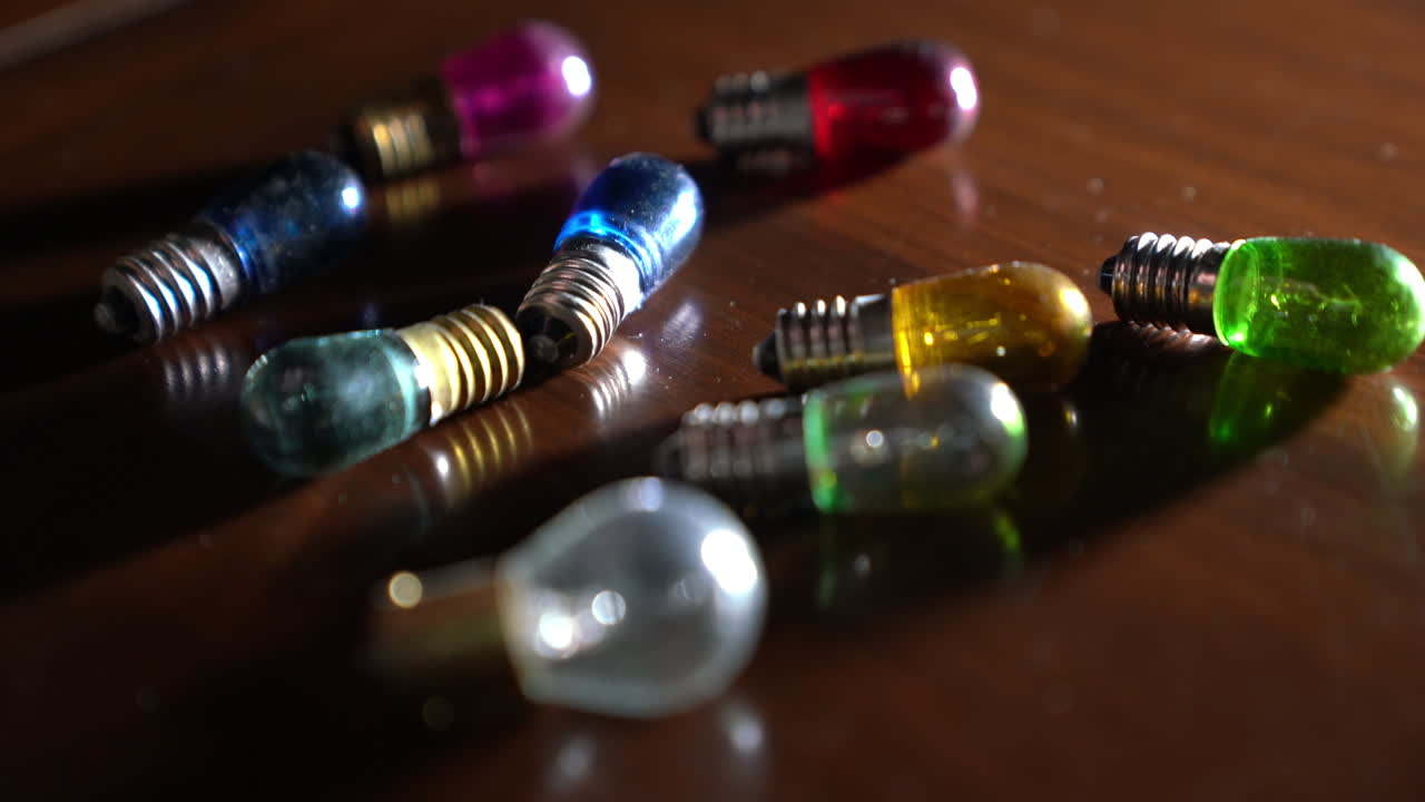 рука человека, который берет со стола цветные разбитые лампочки.