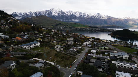 Aerial-drone-panning-shot-over-Queenstown,-New-Zealand-beside-shores-of-the-South-Island’s-Lake-Wakatipu-on-a-cloudy-day