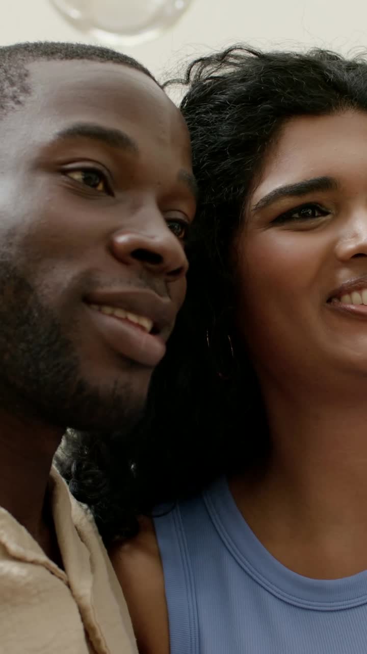 Vídeo vertical: Casal sorrindo, apoiado em casa, enquanto a mulher estende o braço para uma selfie, vestindo bege e azul