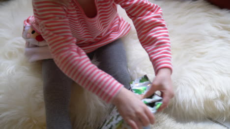 A-child-wraps-a-Christmas-present-on-a-white-fluffy-blanket