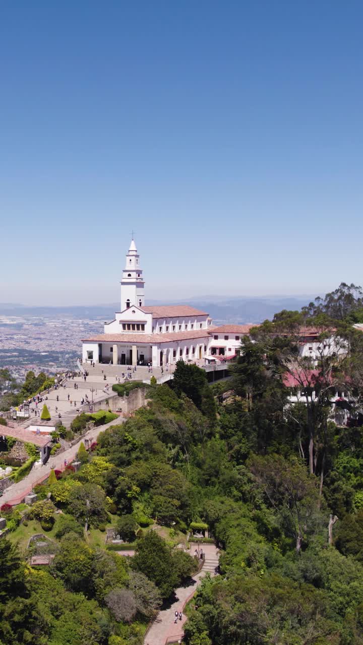 White hilltop church rises over dense Bogotá forest under clear sky, vertical shot