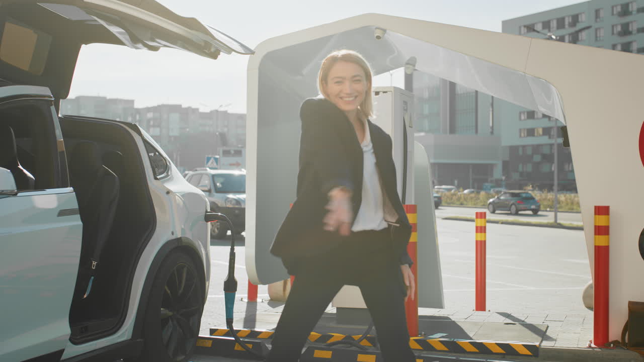 mujer de negocios bailando en una estación de carga de coches eléctricos