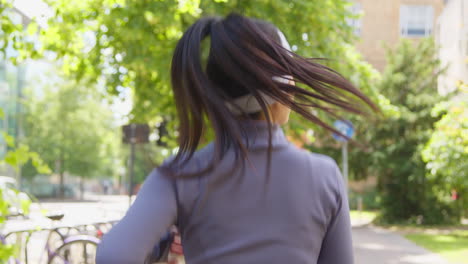 Close-Up-Rear-View-Of-Young-Woman-Exercising-Running-Through-City-Park-Wearing-Wireless-Earbuds