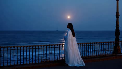 woman in white cape by the ocean at night under the moonlight