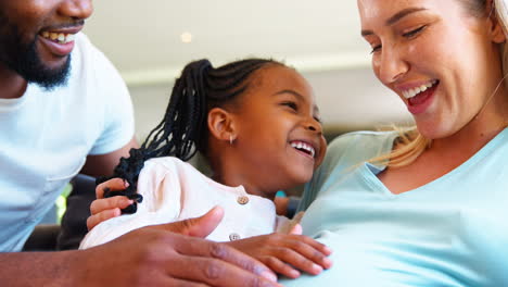 family with daughter cuddling pregnant mother at home together