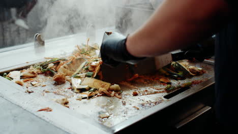 mixing steaming wok dish on festival grill using metal spatula