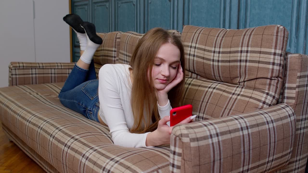 소녀는 모바일 스마트폰 화면을 보고 성공적으로 온라인 주문을 하고, 미소 짓고 카메라를 봅니다.