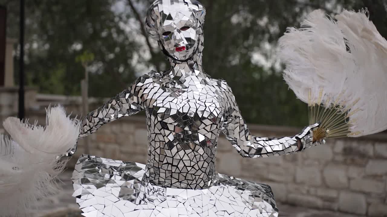 Woman in reflective mirror costume dancing with feather fans. Street performer show.