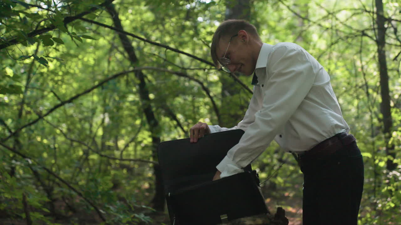 Scientific researcher in white shirt folding white coat, opening backpack and placing coat inside while surrounded by green leaves and sunlight in forest creating calm woodland atmosphere