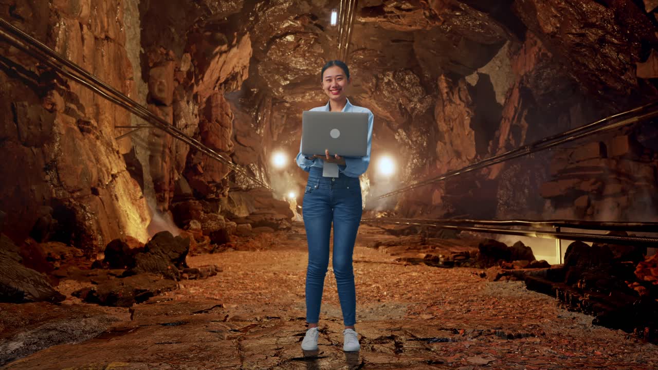 Full Body Of Asian Female With Her Laptop In Underground Mine Tunnel, She Is Looking At The Camera With A Smile