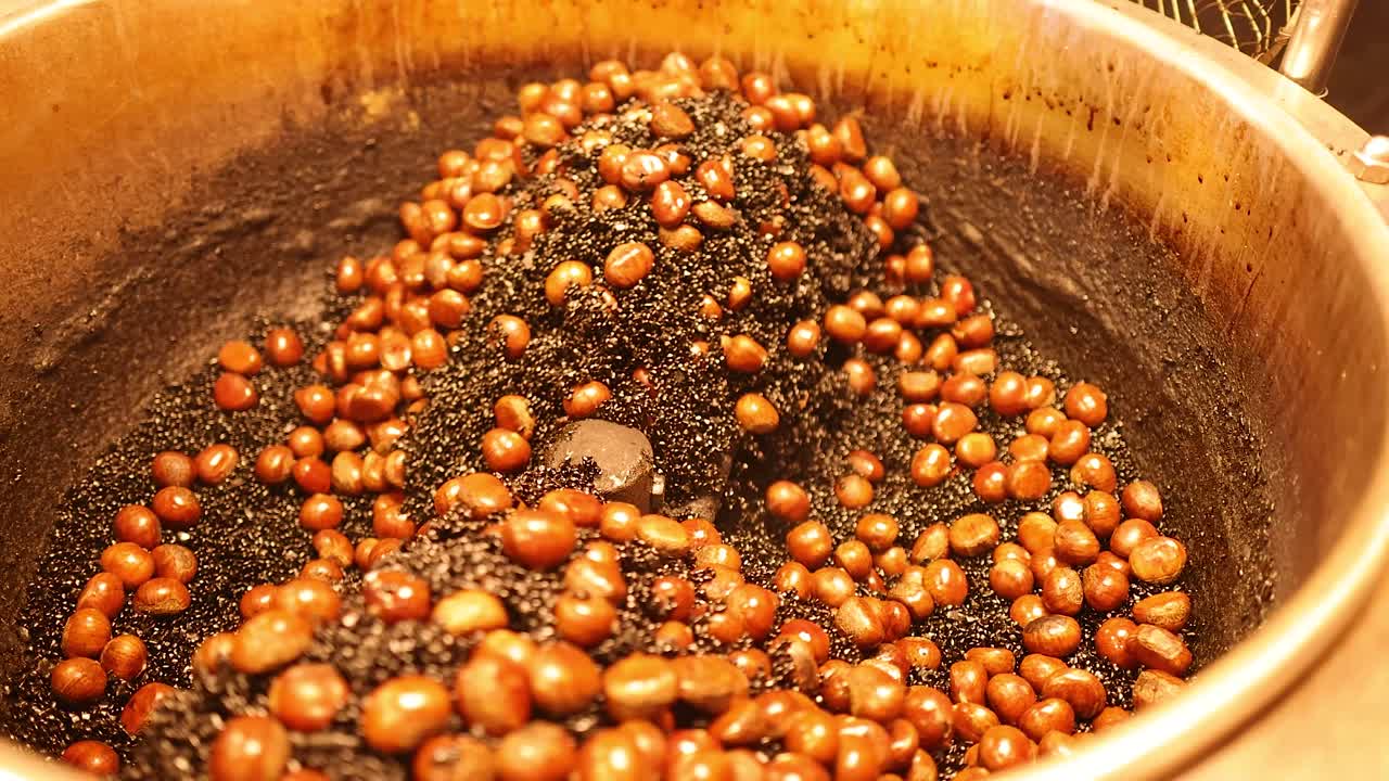 Chestnuts roasting and stirring in hot black sand, warm lighting, close-up, street food scene